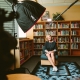 Lachende vrouw zittend in een kamer vol boeken met een camera op zich gericht voor het maken van een documentaire.